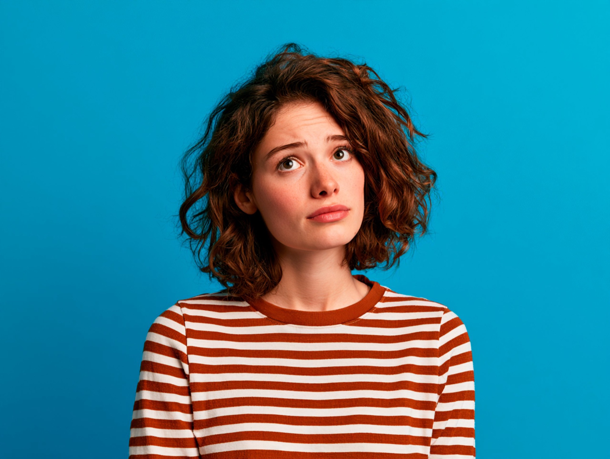 Vrouw in een gestreepte trui kijkt twijfelend opzij tegen een blauwe achtergrond